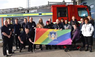 Staff and firefighters stood in front of a Fire Engine holding up a Fire Pride flag.